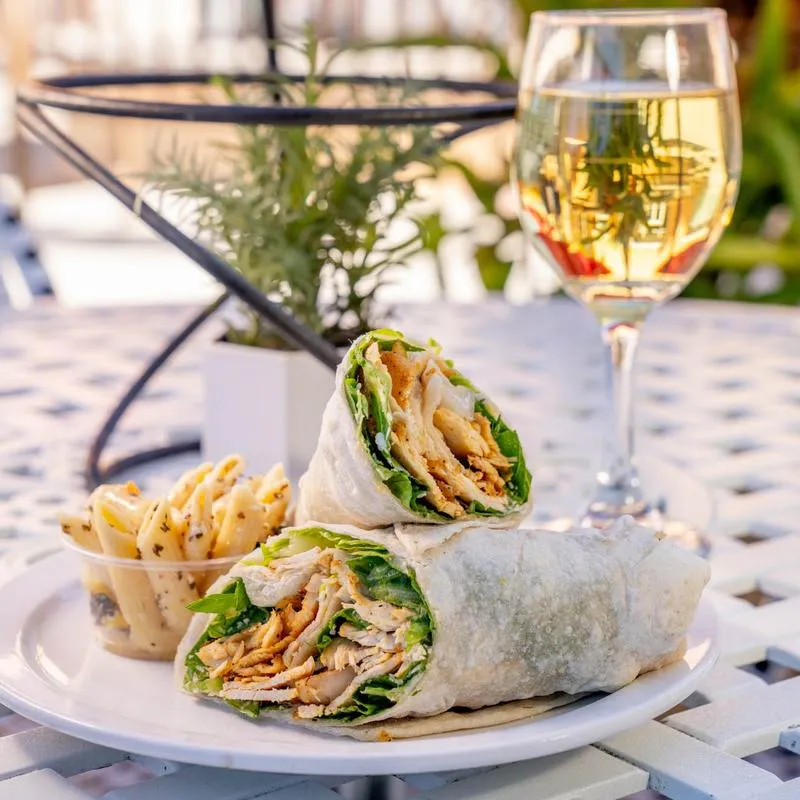 Chicken Caesar wrap served with pasta salad and a glass of white wine.