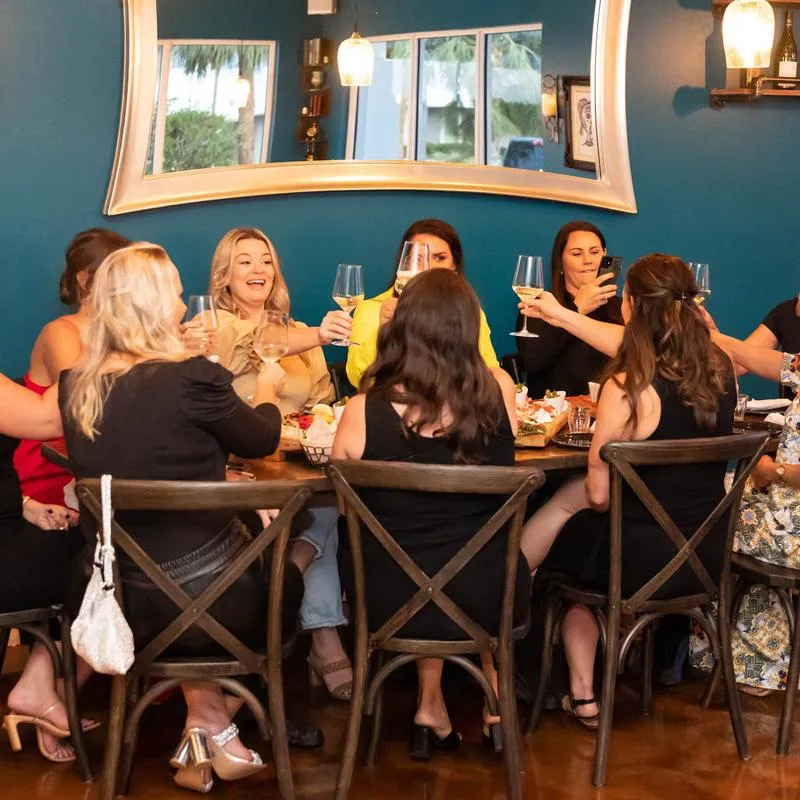 Interior, customers making a toast, chairs, table, decorative mirror, bottles on shelves