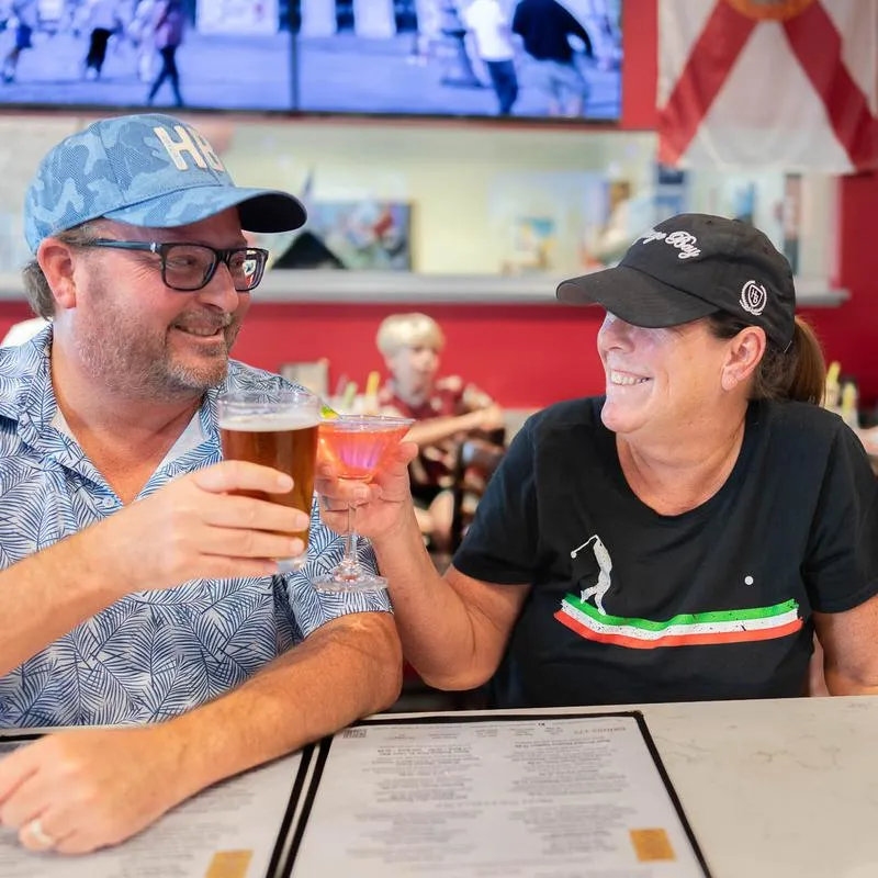 Two people laughing and toasting drinks at a bar.