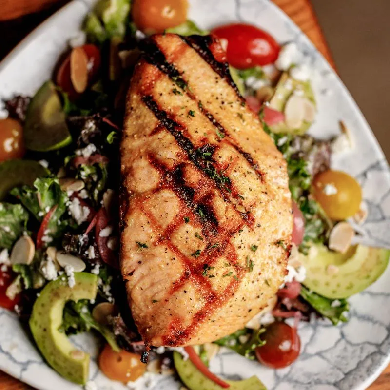 Grilled salmon salad with greens, avocado, cherry tomatoes, cheese, and almonds.