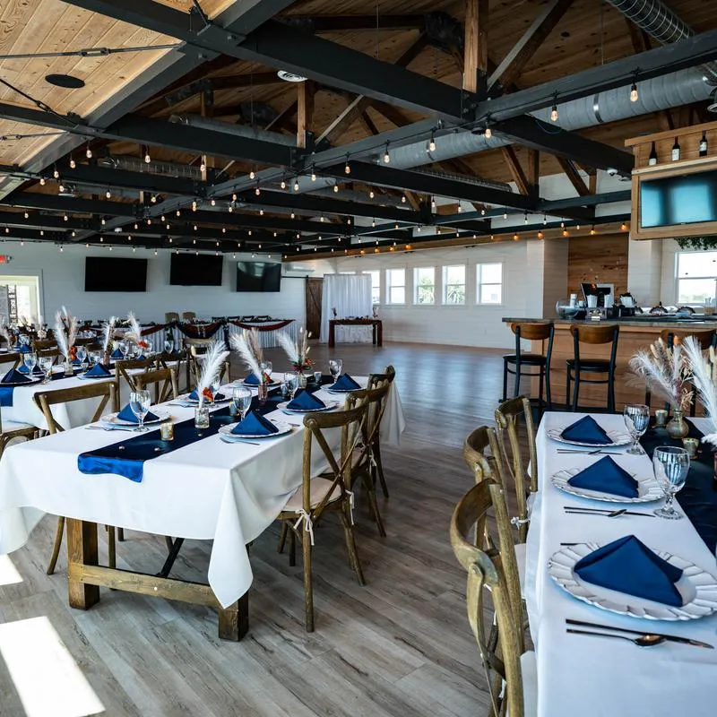 An elegant interior - tables set with white tablecloths, navy napkins and pampas grass; string lights.