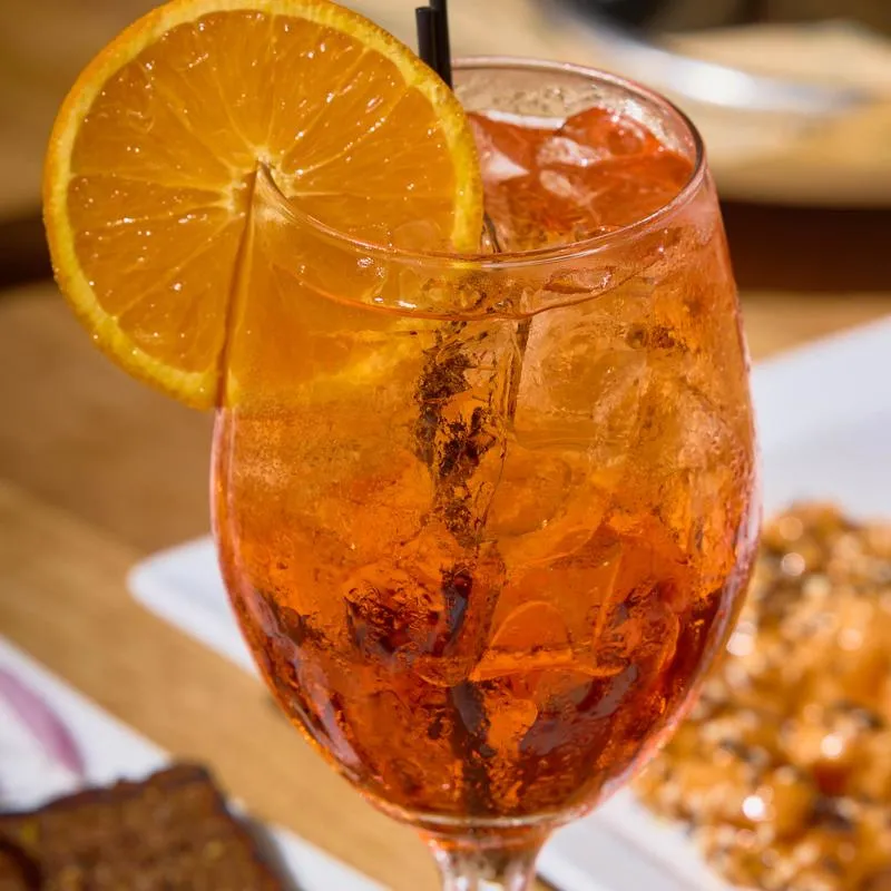 An orange-hued Italian cocktail with prosecco, Aperol, soda, ice, and citrus garnish.