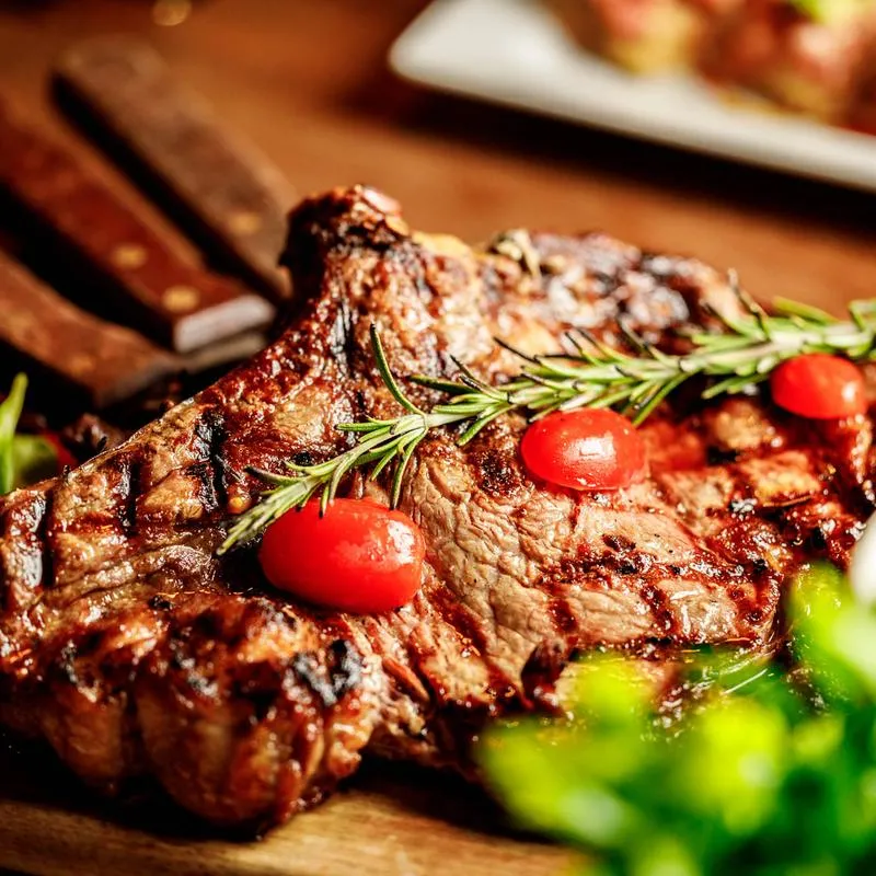 Grilled ribeye steak garnished with rosemary and cherry tomatoes.