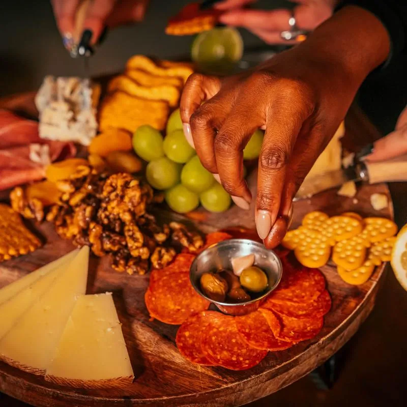 A hand picking food from a cheese and charcuterie board