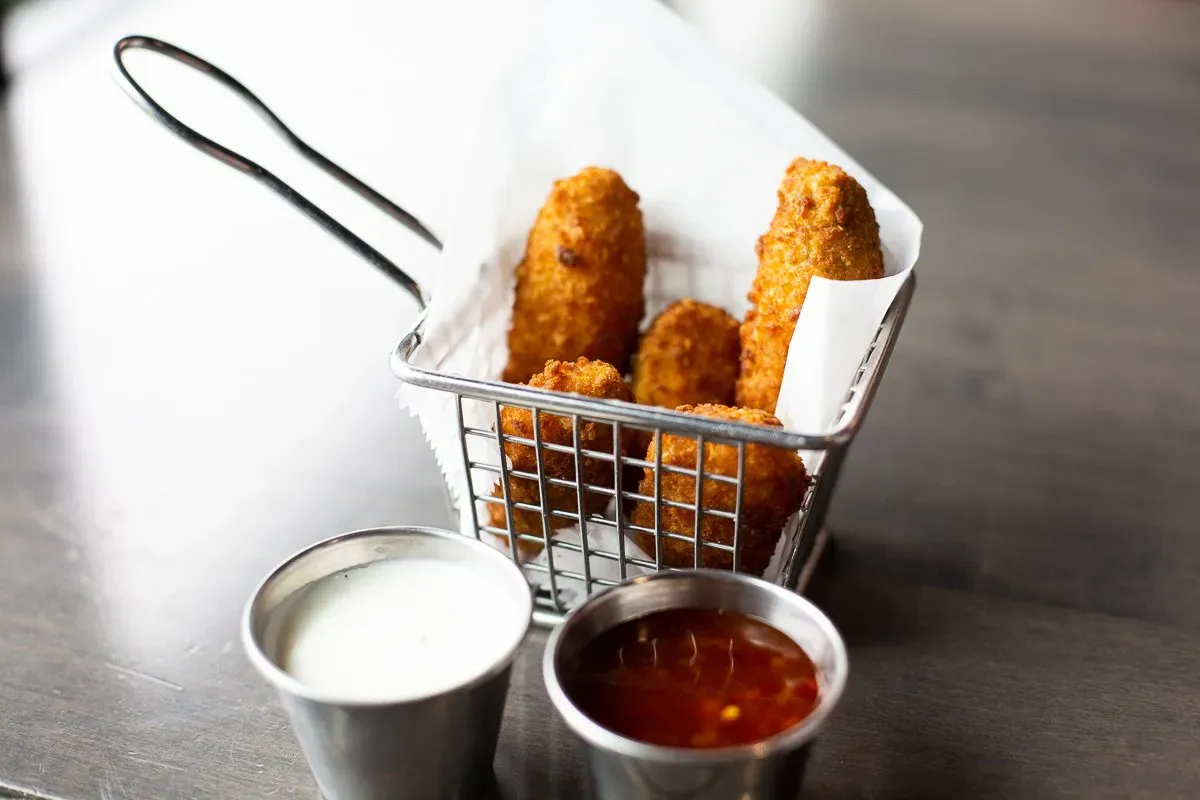 A basket of mozzarella sticks with dipping sauces on a table.