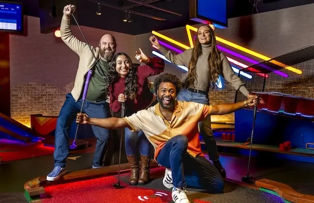 Group posing with mini golf putters on an indoor mini golf course during a group event