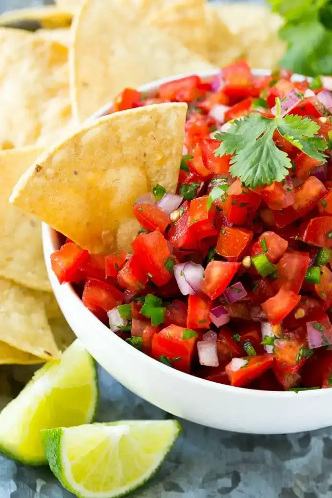 Bowl of fresh pico de gallo with tomatoes, onions, cilantro, and jalapeños, served with tortilla chips and lime wedges.