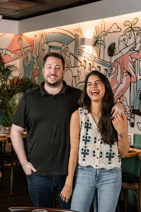 Fede and Eva, the owners, standing in front of the mural in the dining room
