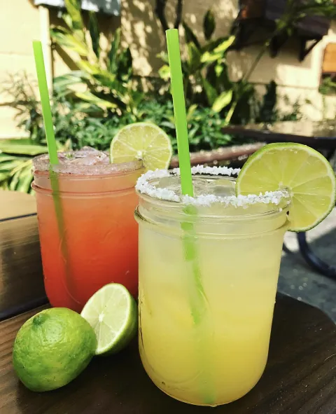 a red margarita and a green margarita on an outside table, a lime cut open in front of the margaritas
