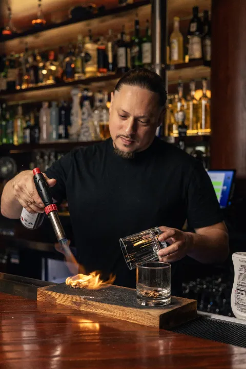 Bartender torching cocktail glass with blowtorch