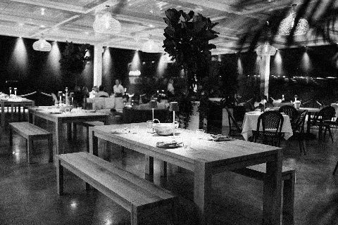 Elegant black and white interior of Lamarina waterfront restaurant in West Palm Beach featuring wooden tables and benches, atmospheric hanging lights, and sophisticated coastal dining ambiance