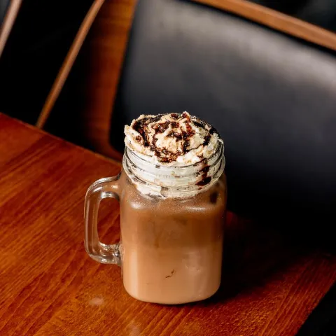 Iced coffee topped with whipped cream served on a wooden table.