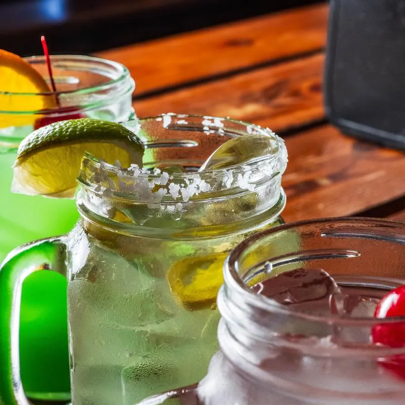 Close-up of cocktails in mason jars with citrus and cherry garnishes.