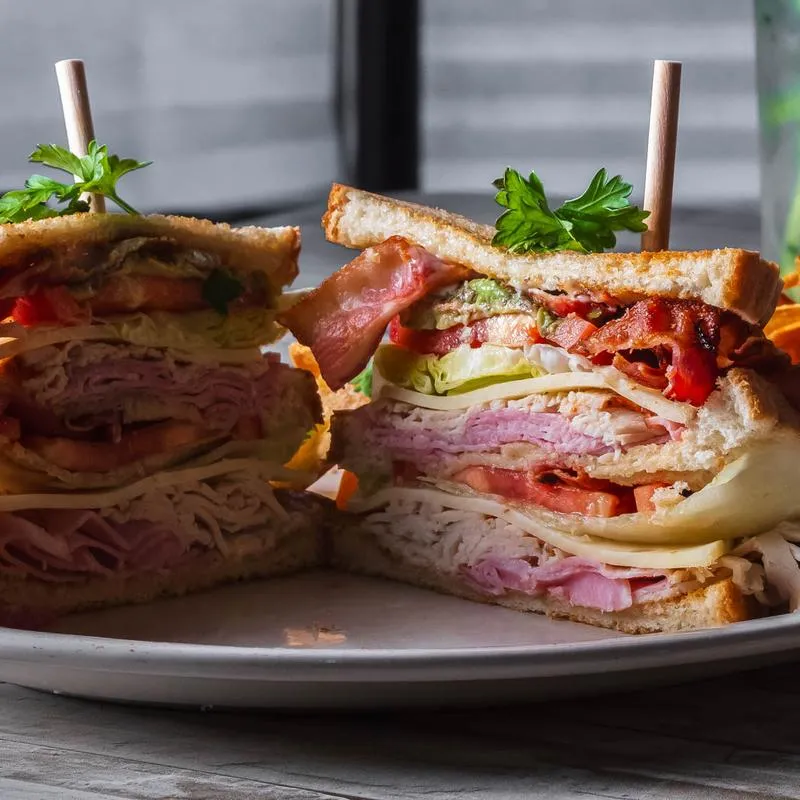 Stacked club sandwich with lettuce, tomato, ham, cheese, and bacon.