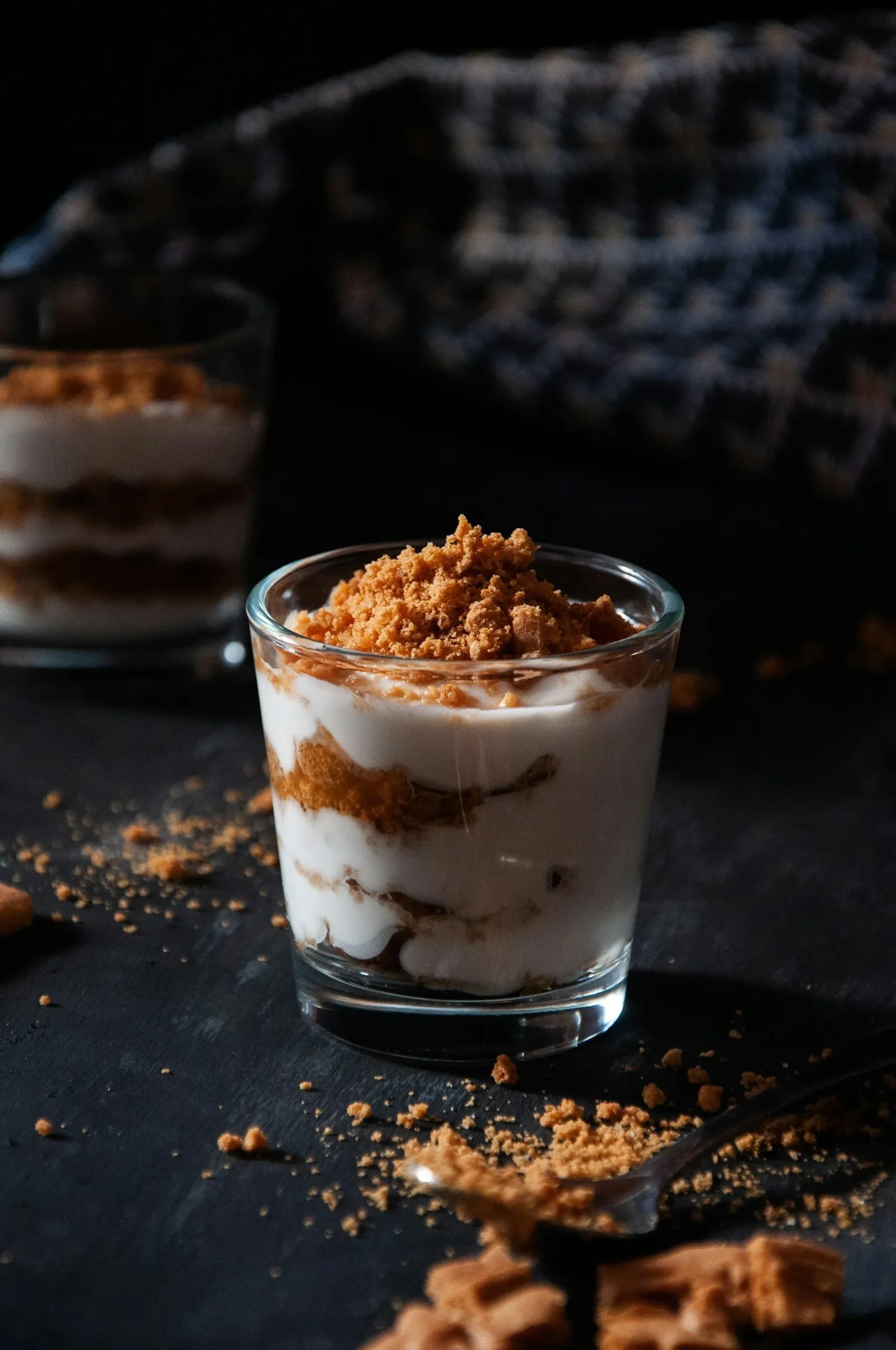 A glass of layered cheesecake with graham cracker crumbs and whipped cream