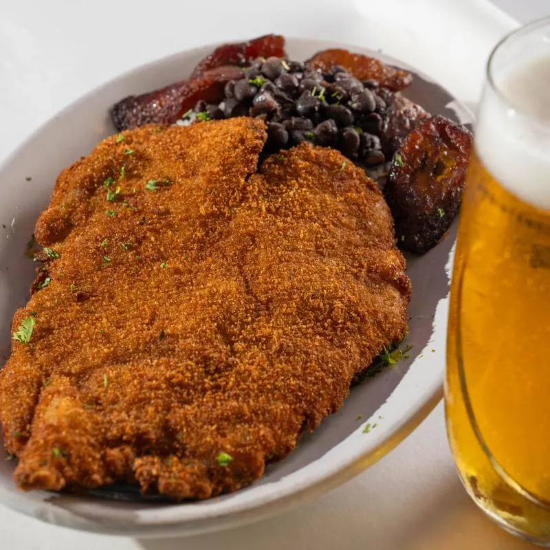 Palomilla Steak served with rice and black beans, accompanied with a glass of beer.