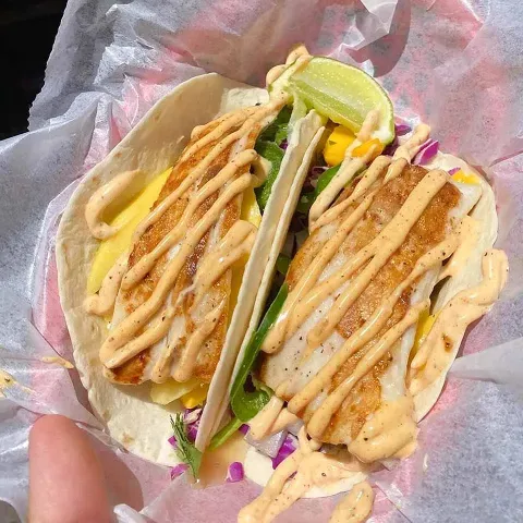 Enjoy two delicious fish tacos in flour tortillas, filled with fresh greens, zesty lime wedges, and finished with a creamy sauce drizzled on top.