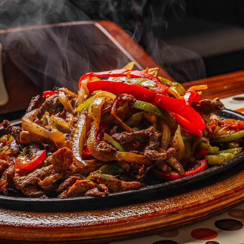 Chicken and steak fajita with onions and bell peppers, served in a skillet.