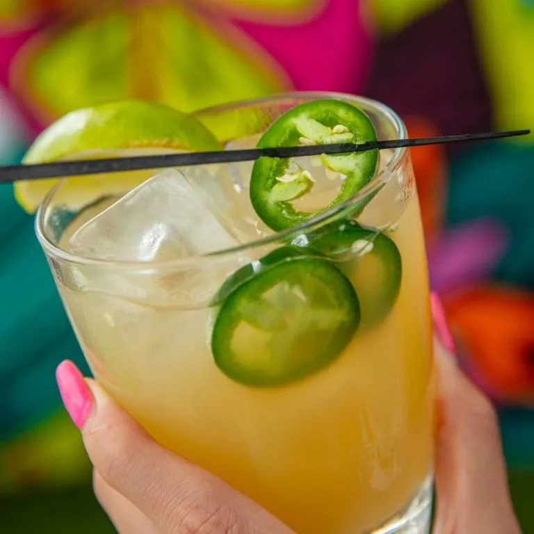 A Hand Holding A Glass Of Green Liquid With Limes In It