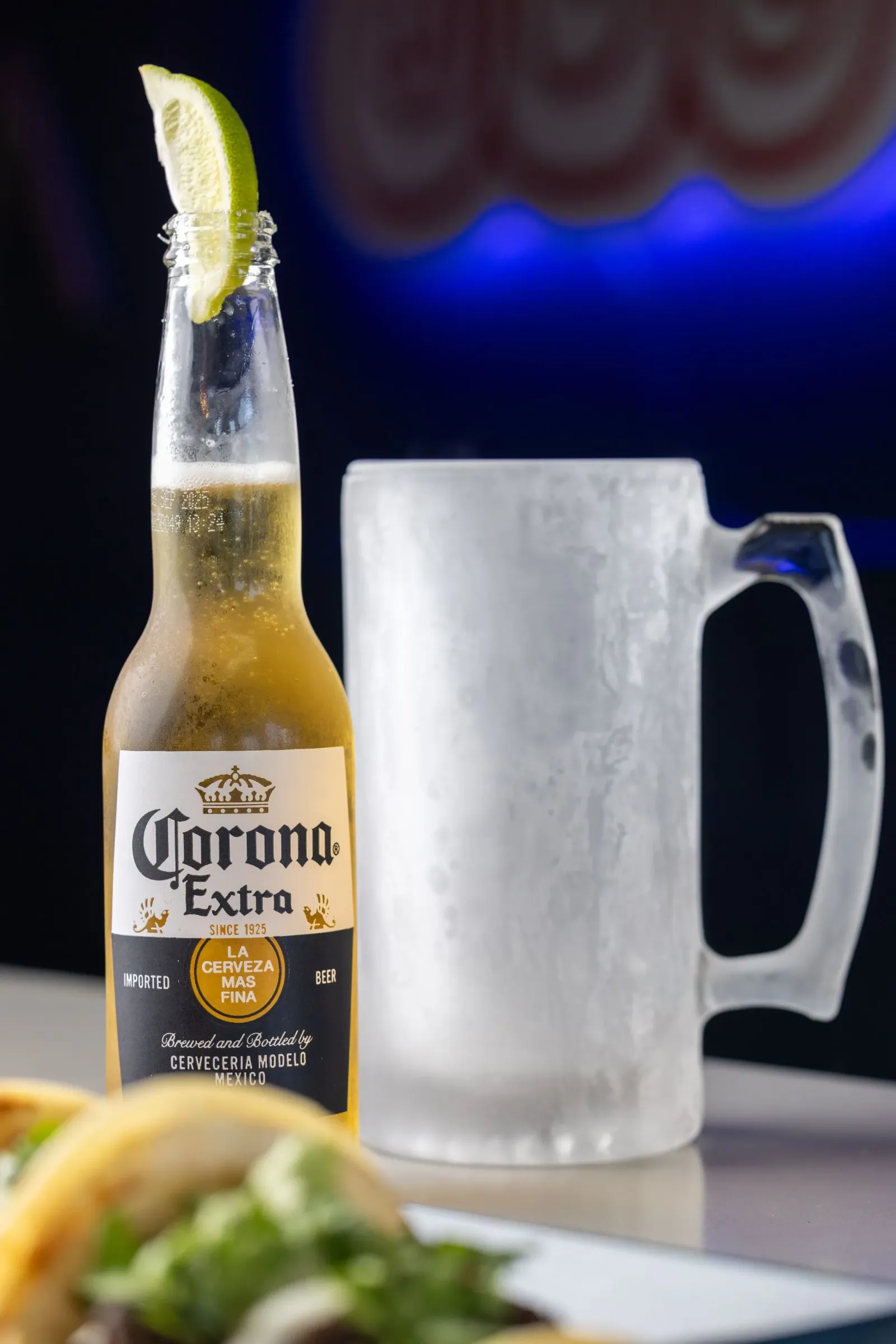 Corona beer bottle with lime wedge, frosted mug, tacos.