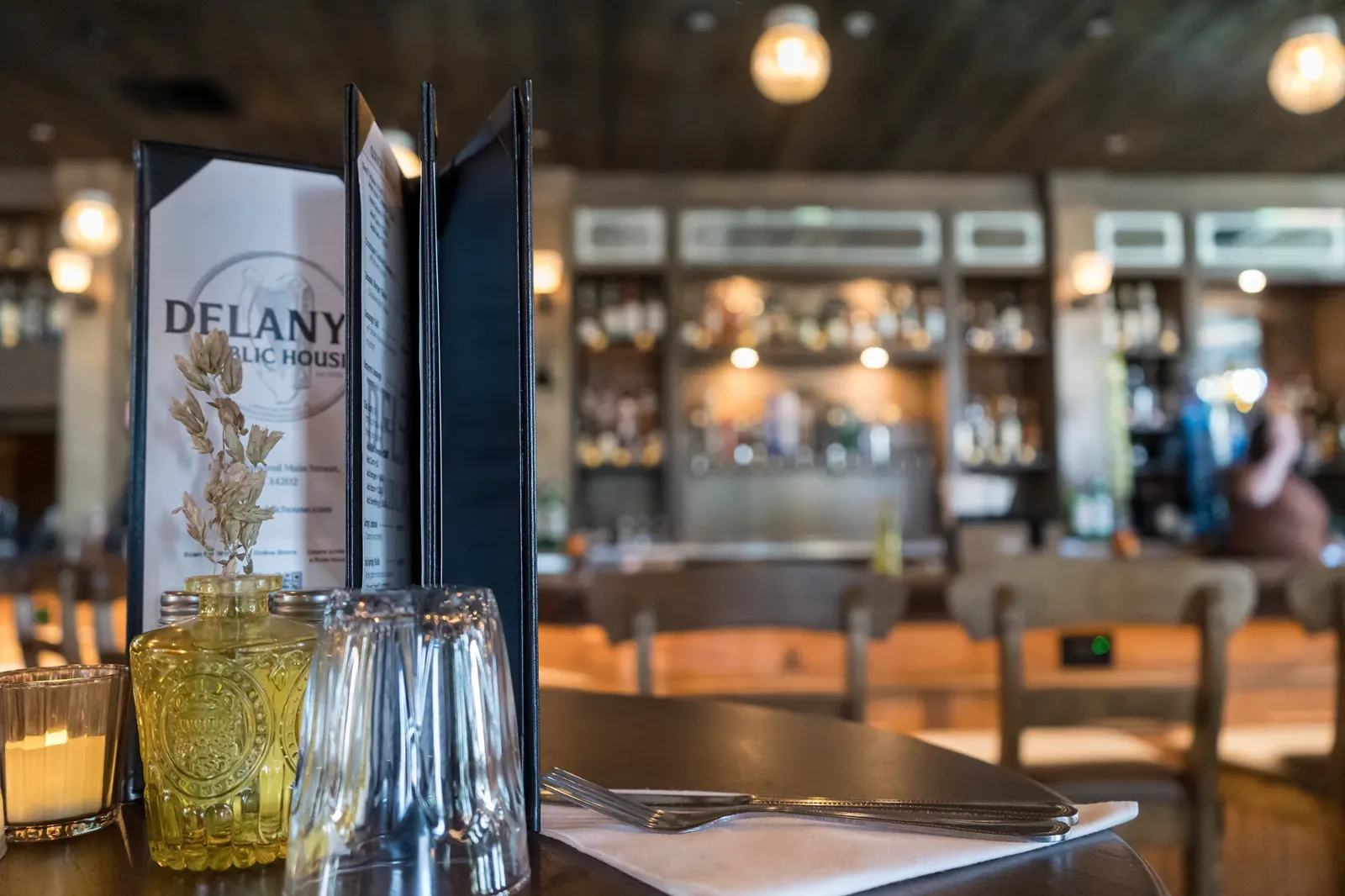 Delany's menu beside flowers and glassware, with the bar in the background.
