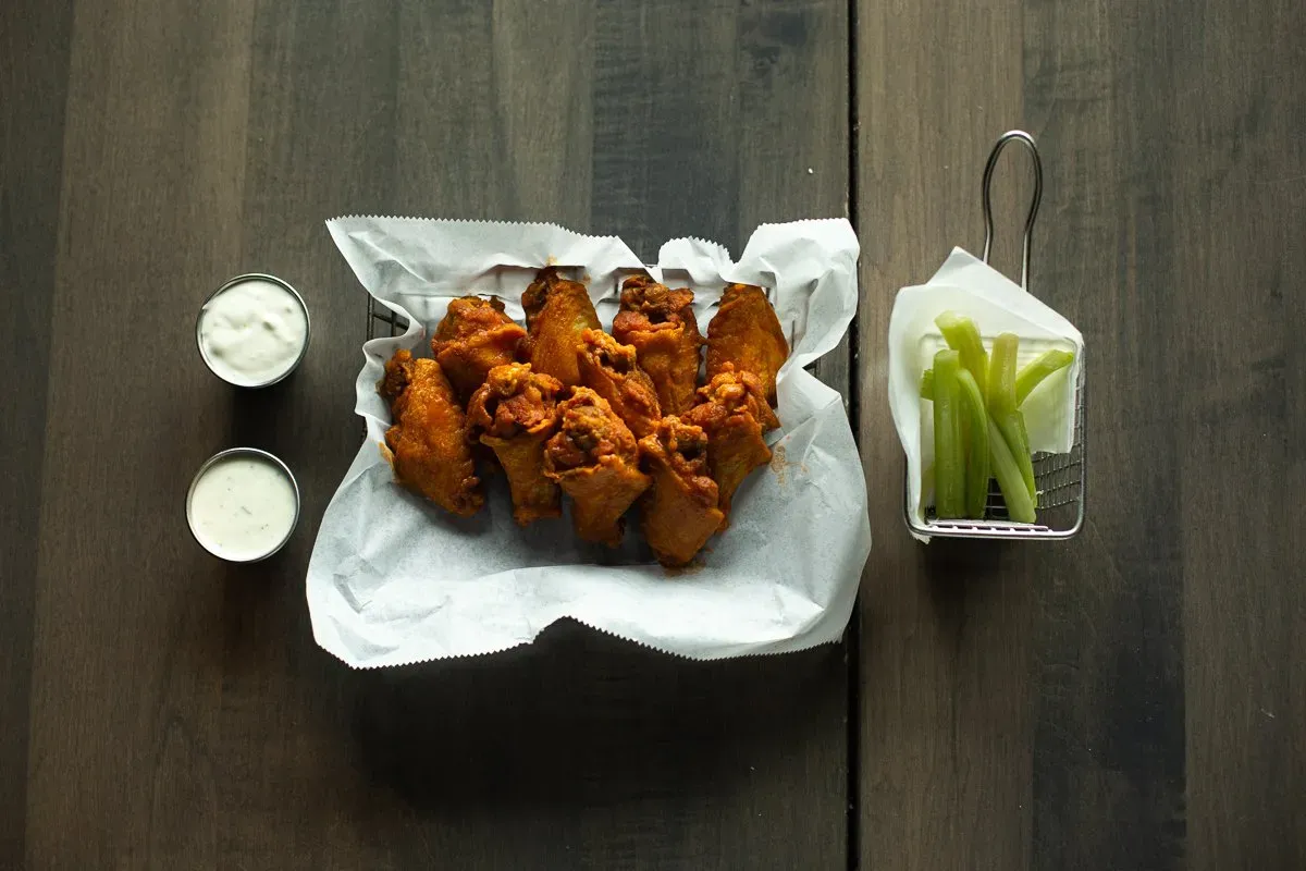 A basket of chicken wings and celery sticks on a wooden table.