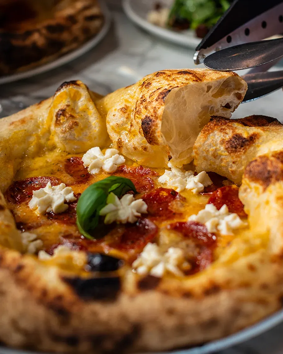 Image of Pizza with pepperoni, basil and whipped cheese being cut with scissors