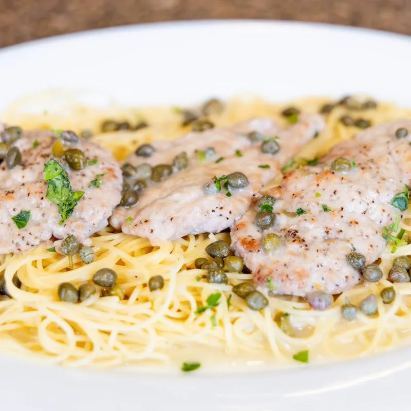 Chicken piccata served over pasta with capers.