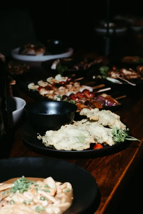Assorted Japanese dishes, including tempura, sushi, and ramen, served on black plates and bowls on a wooden table.