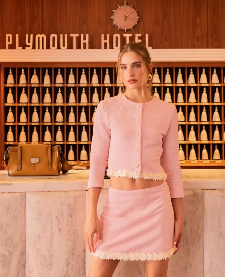 Woman in a pink skirt set posing in front of the signature retro lobby key wall at The Plymouth Hotel South Beach
