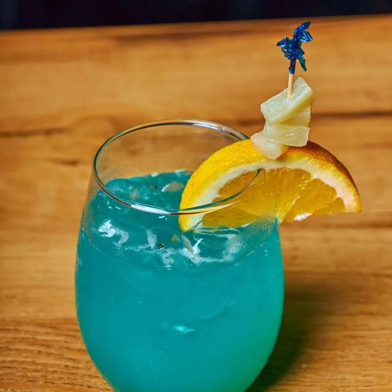 A blue cocktail drink glass garnished with lemon wedge.