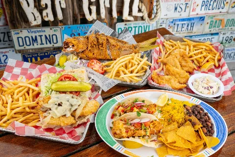A spread of Hogfish Bar & Grill dishes, fried whole snapper, the Killer Hogfish Sandwich, fish and chips, and Baja-style tacos