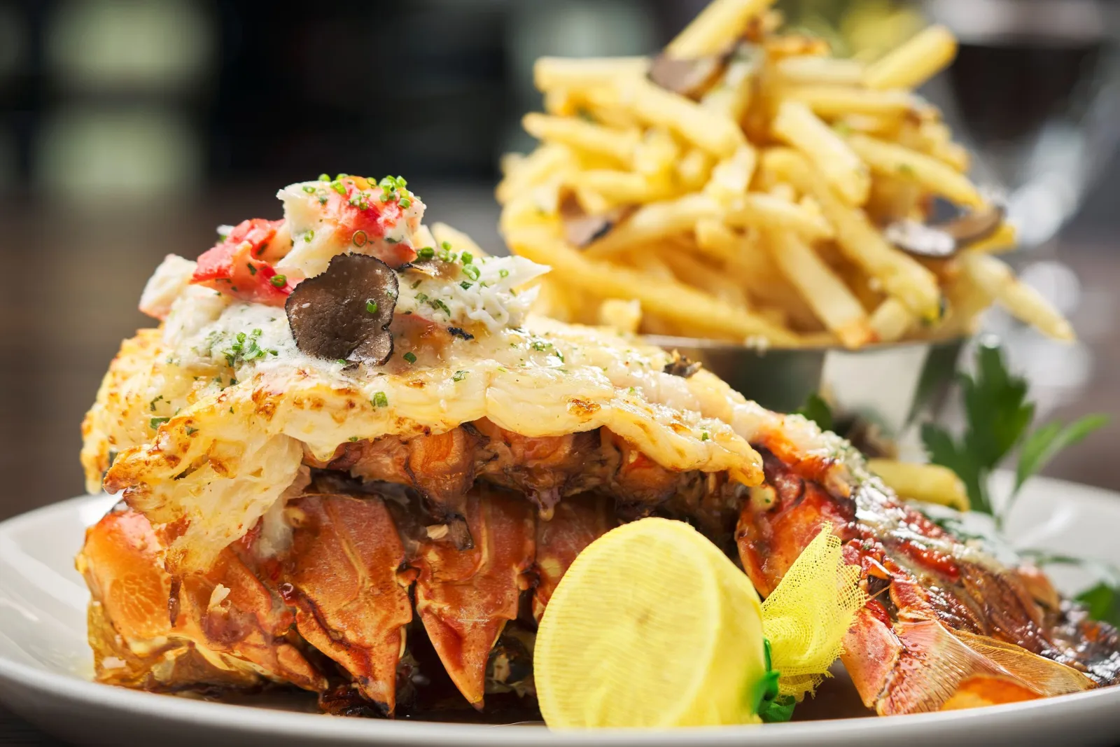 Lobster frites featuring a roasted lobster tail topped with butter and chives, served with crispy golden fries and lemon.