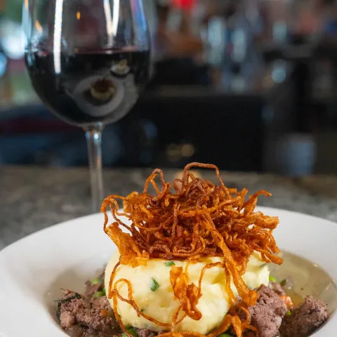 Cooked beef topped with mashed potatoes and crispy shoestring onions, paired with red wine.