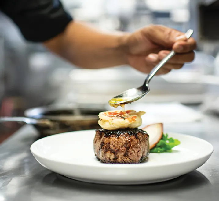 Chef pouring butter on top of a steak dish