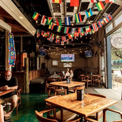 Gastropub interior with polished wooden tables, string lights, and international bunting banners.