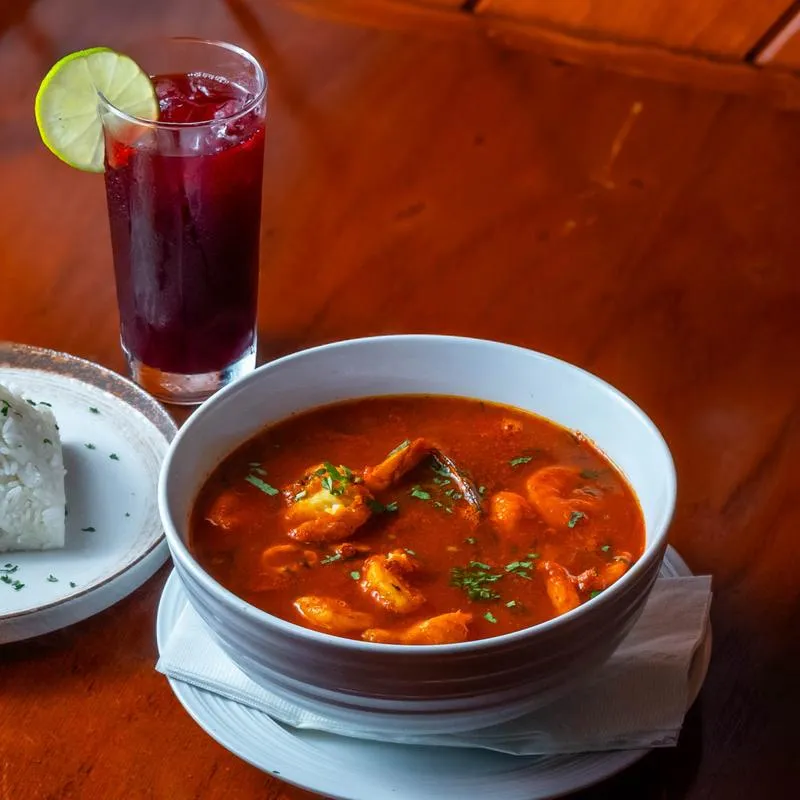 Bowl of spicy shrimp soup served with a berry cocktail and rice.