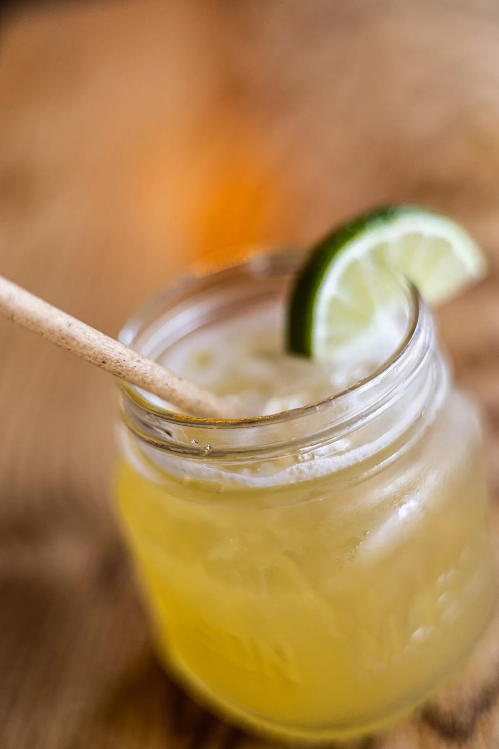 Lemonade in a glass jar with lime and lemon slices, ice, and a straw, placed on a wooden surface.