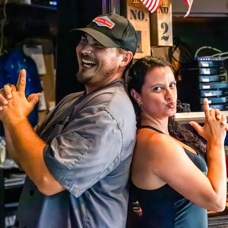 Two individuals posing back-to-back in a bar setting.