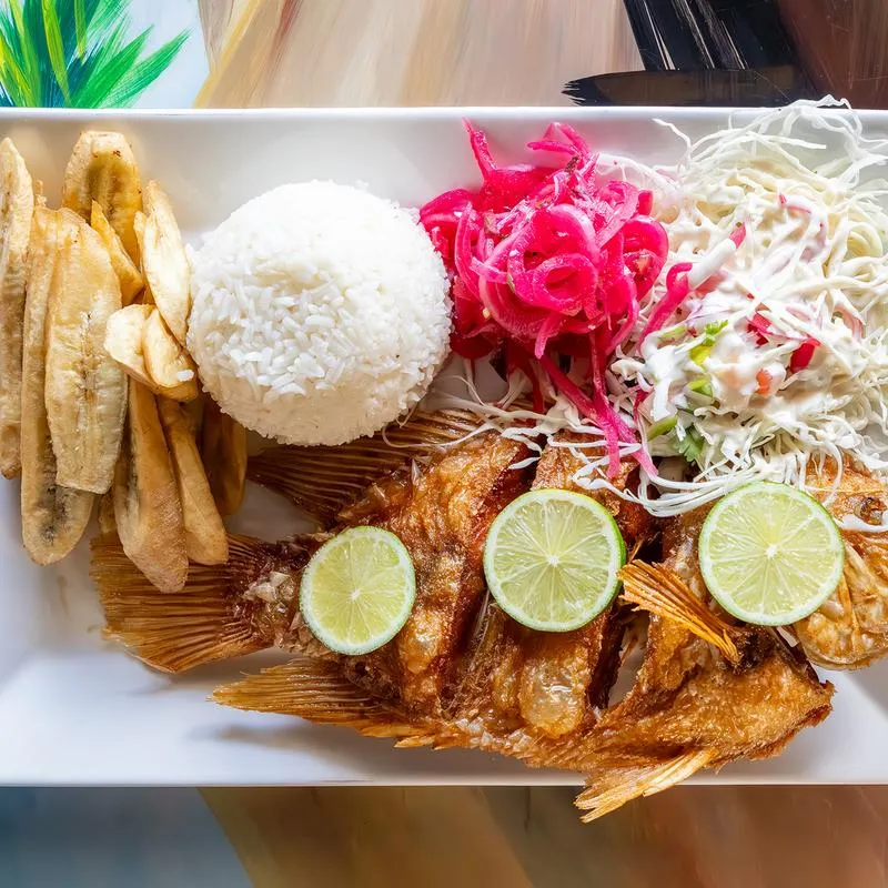 Fried tilapia fish, with rice, fried plantains, pickled red onions, and cabbage salad.