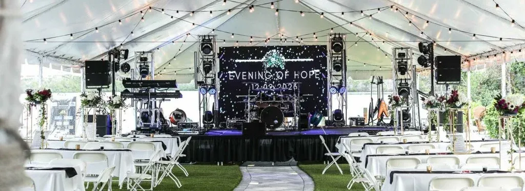 private event tent on the lawn with waterfront view of Lemon Bay. Strings of lights, a band platform, tables, chairs, and floral centerpieces