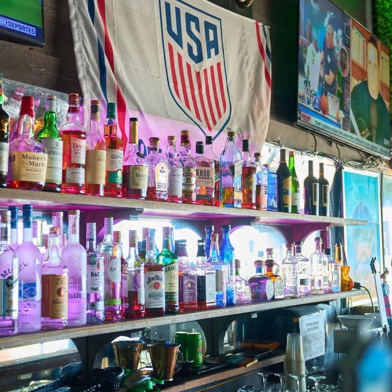 Well-stocked bar counter with rows of liquor bottles on shelves.