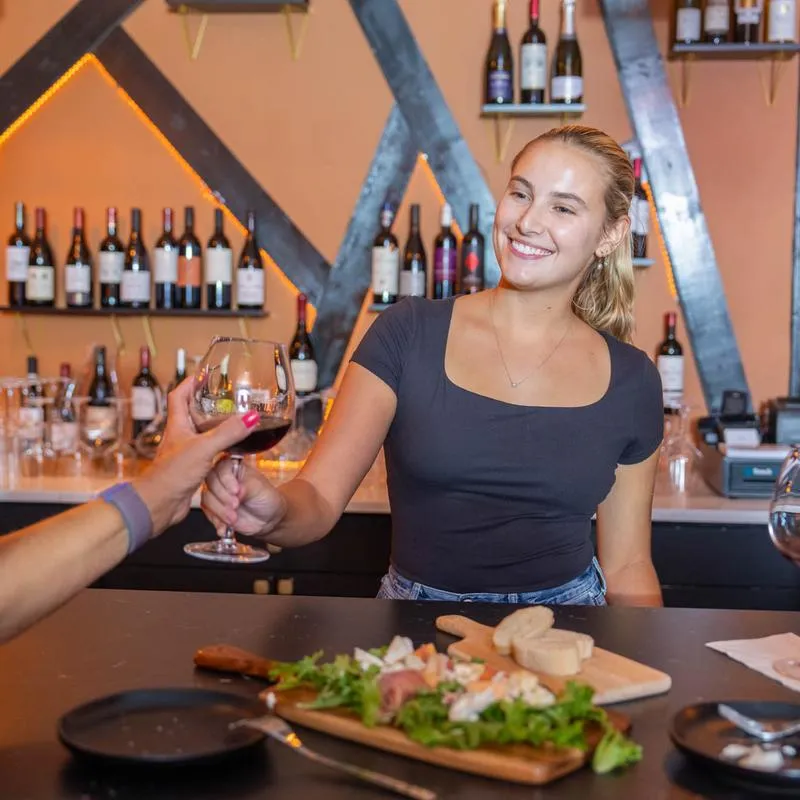 A friendly bartender serves wine to a customer at a counter.