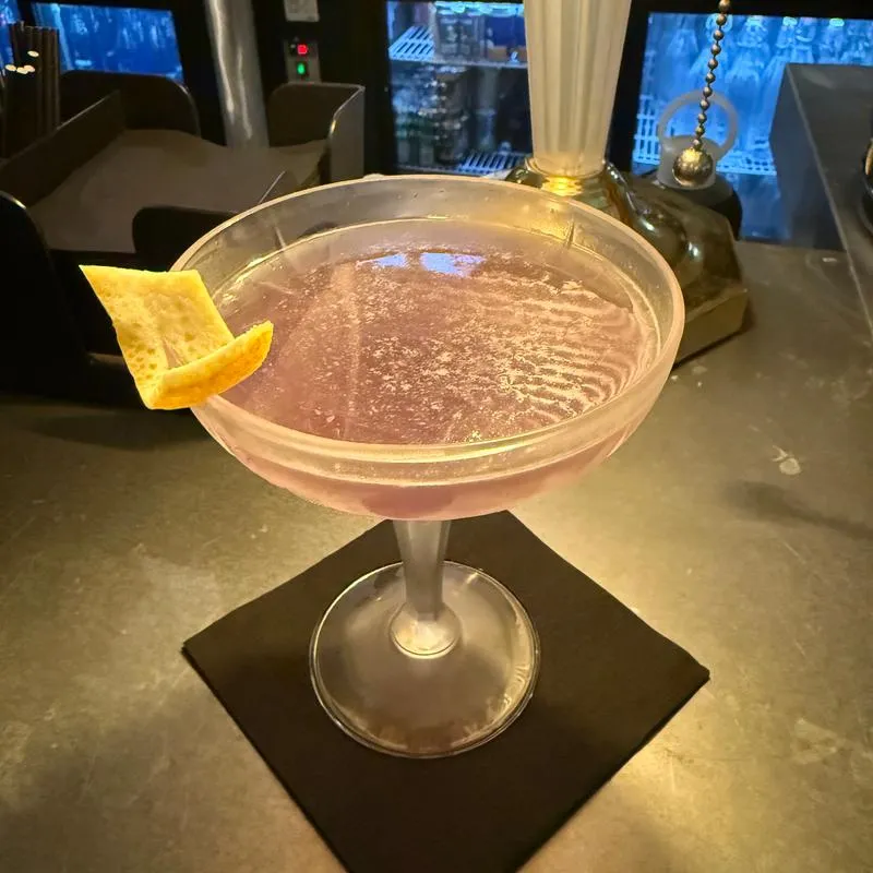 Cocktail served in a coupe, garnished with a orange peel.