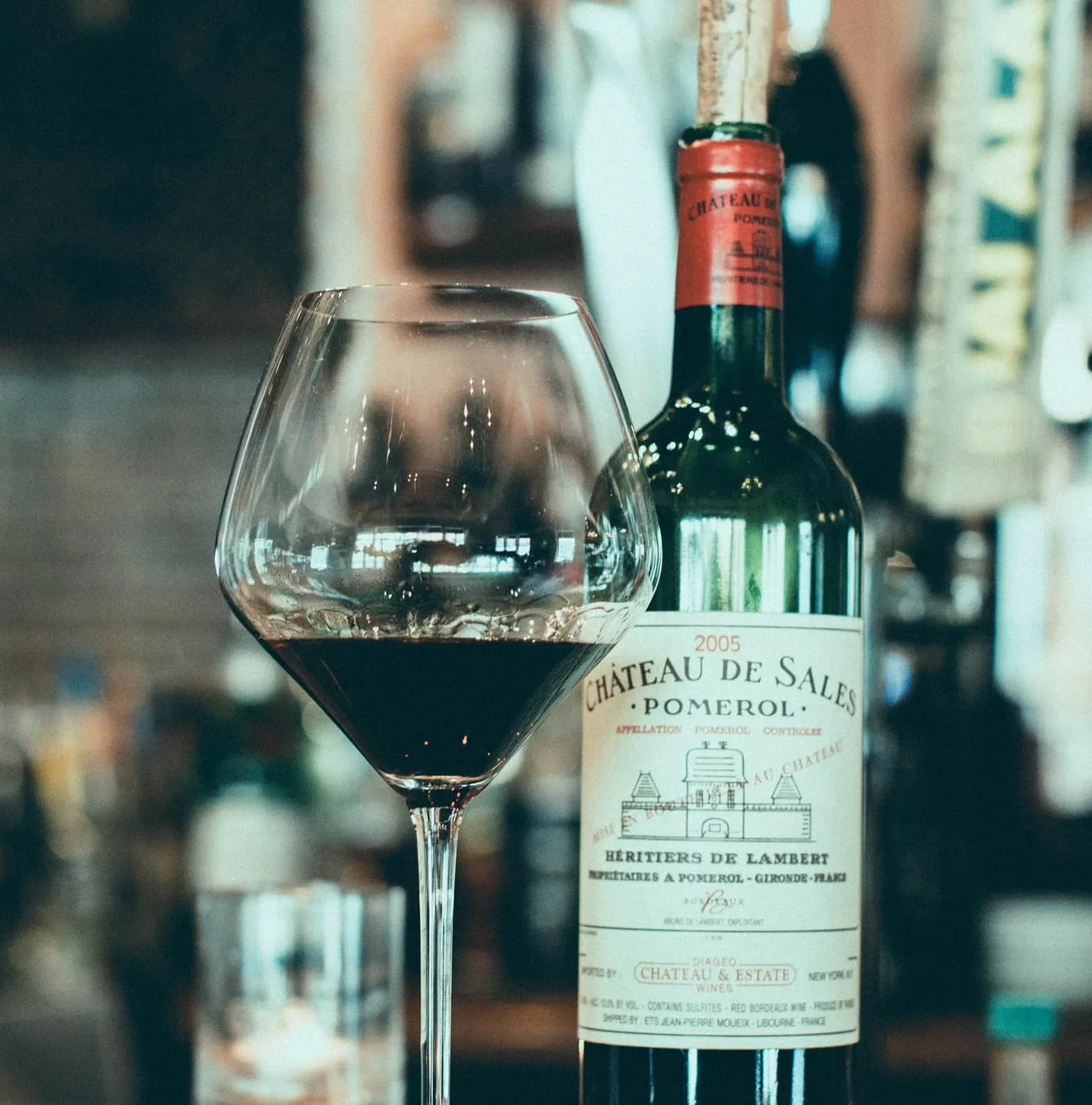 Glass of red wine with Chateau de Sales Pomerol bottle in background.
