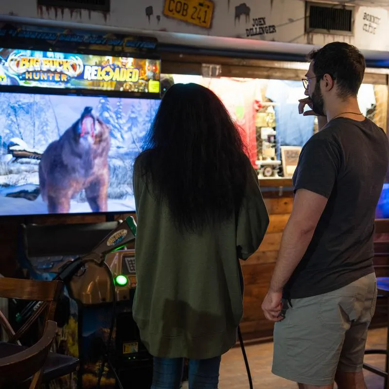 Two people playing arcade hunting game in a bar.
