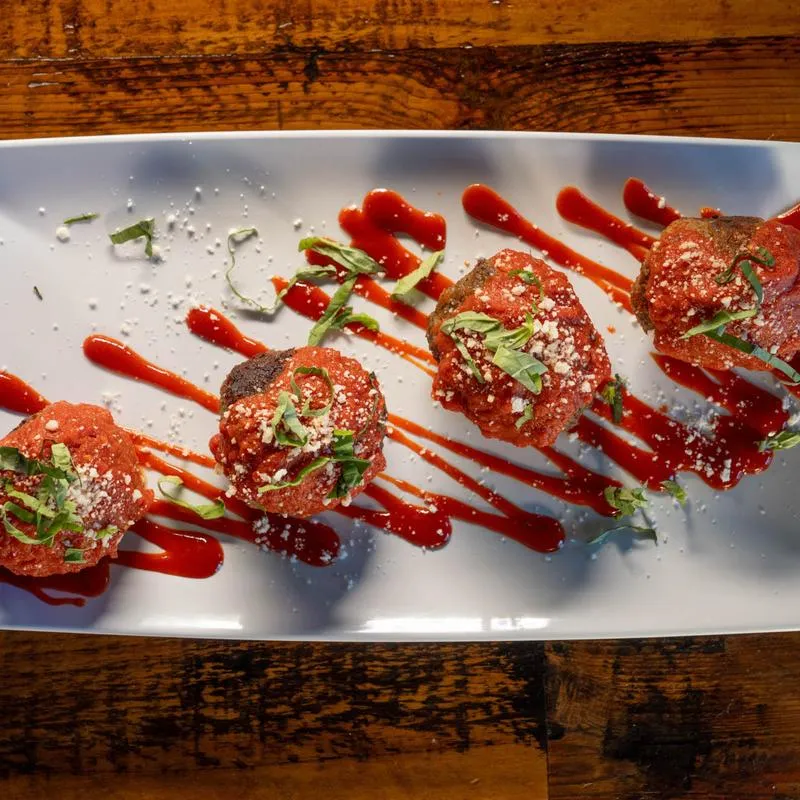 Plate of meatballs topped with red sauce drizzle, grated cheese, and herbs.