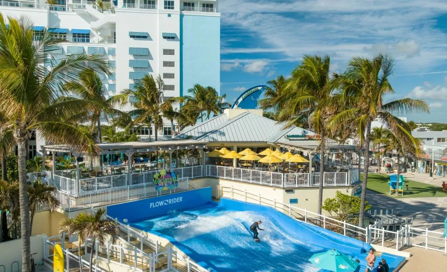 A Pool With People In It By A Beach And Buildings