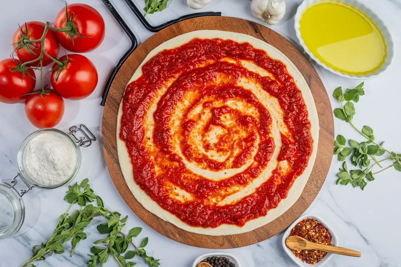 Fresh, never frozen pizza dough topped with tomato sauce and surrounded by fresh ingredients