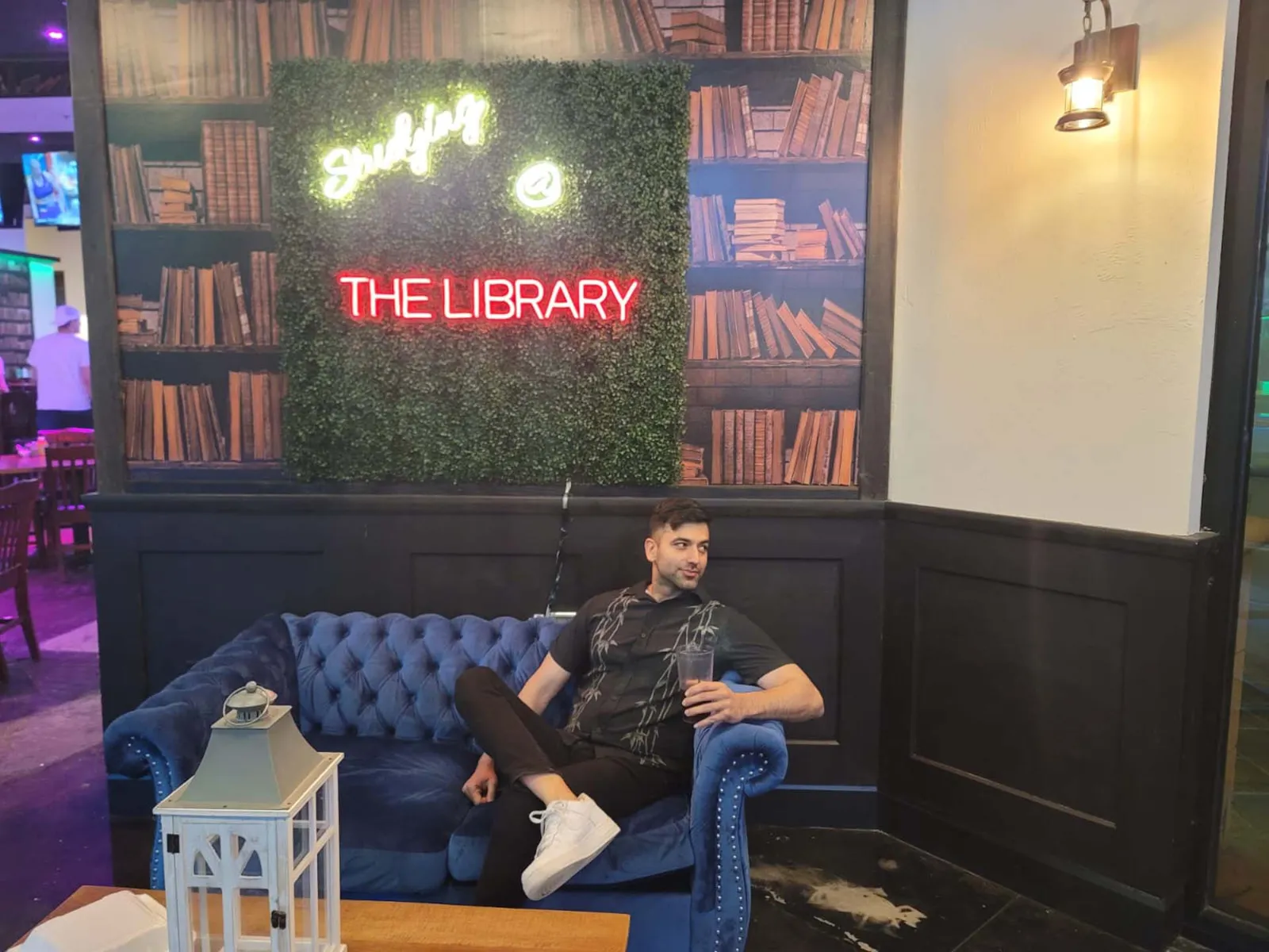 a man sitting in a couch and a bookshelf stamp on the wall is behing him